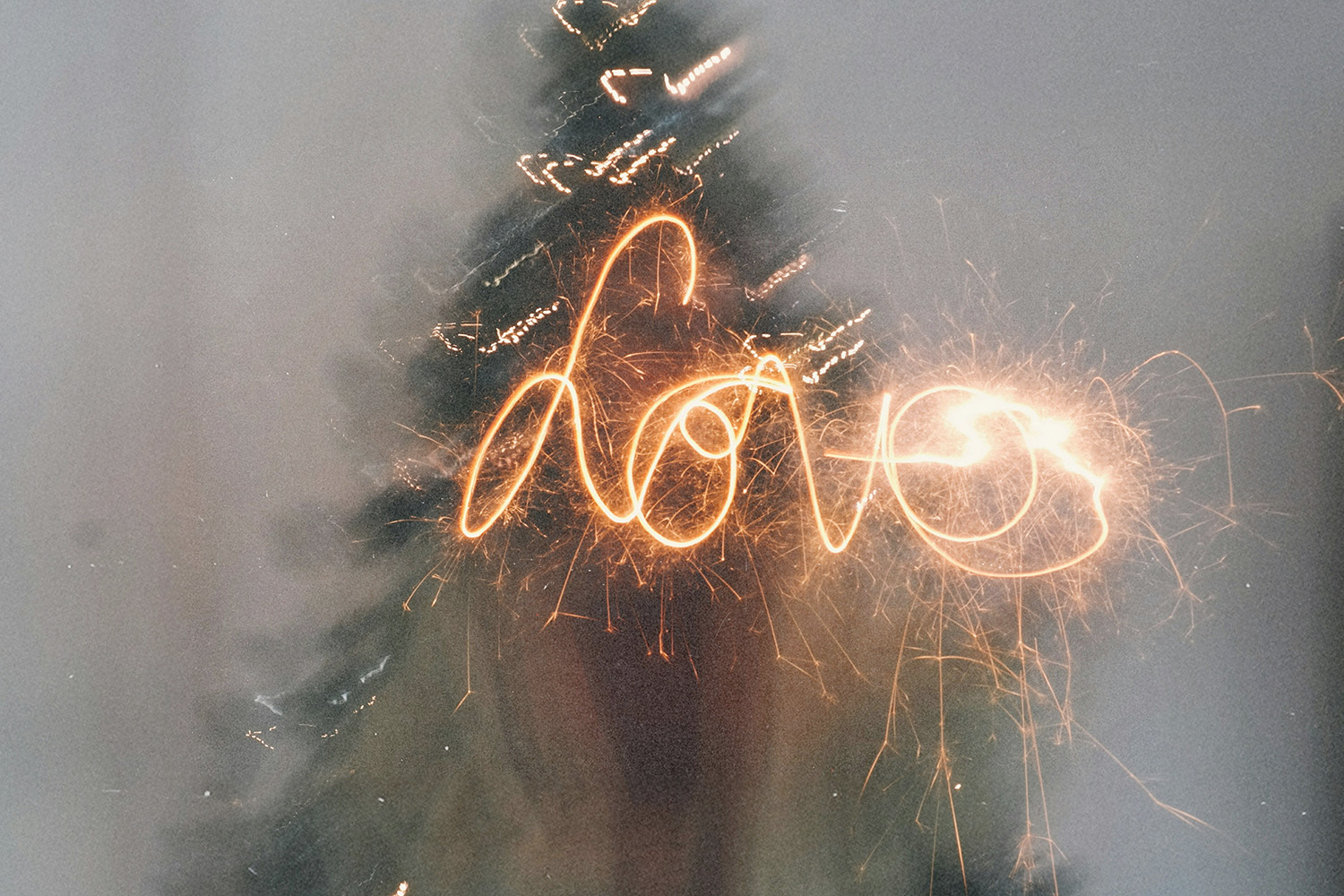 Sparkler light spelling ‘love’ in front of a blurred Christmas tree, creating a festive glow.