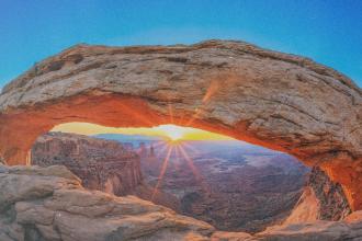 Canyon Landscape with the sun setting on the horizon. The sun is under a rock archway