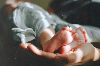 Close-up of newborn feet resting in a caring hand, reflecting God’s Gift of life, the true Christmas gift, and the hope found in God’s Plan for us all.