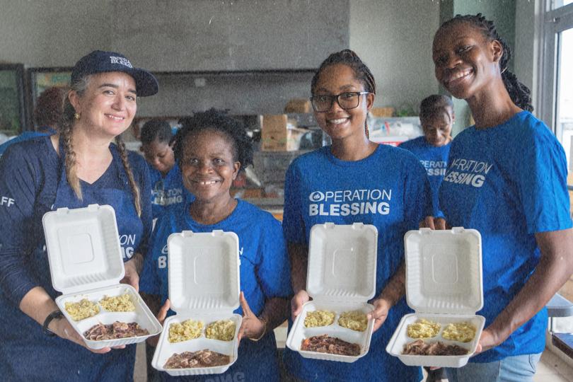 Operation Blessing team holding meal boxes with rice and meat, supporting local communities with food assistance.